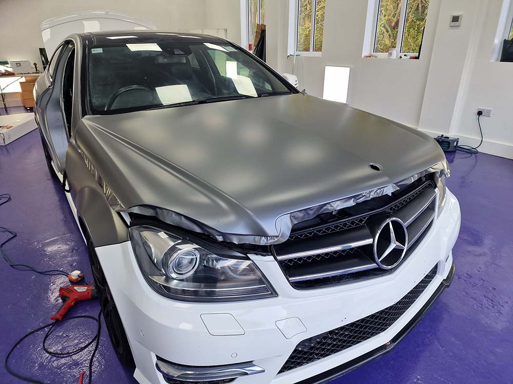 Satin grey vinyl being fitted to the Mercedes bonnet with the headlights removed